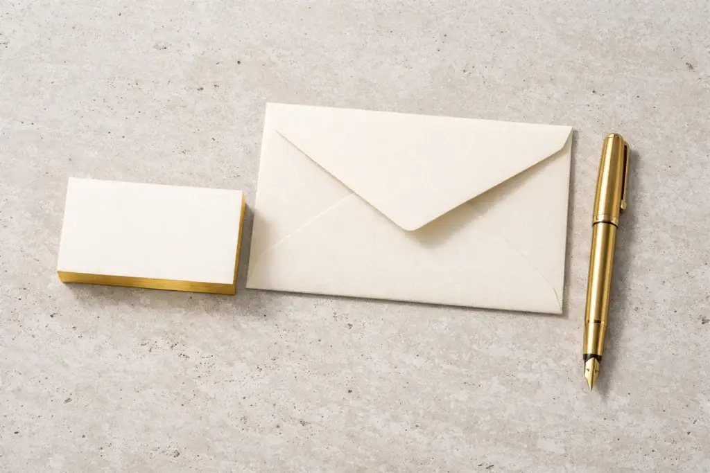 Cream business cards and envelope with a gold fountain pen on a neutral stone background, minimalist luxury stationery mockup